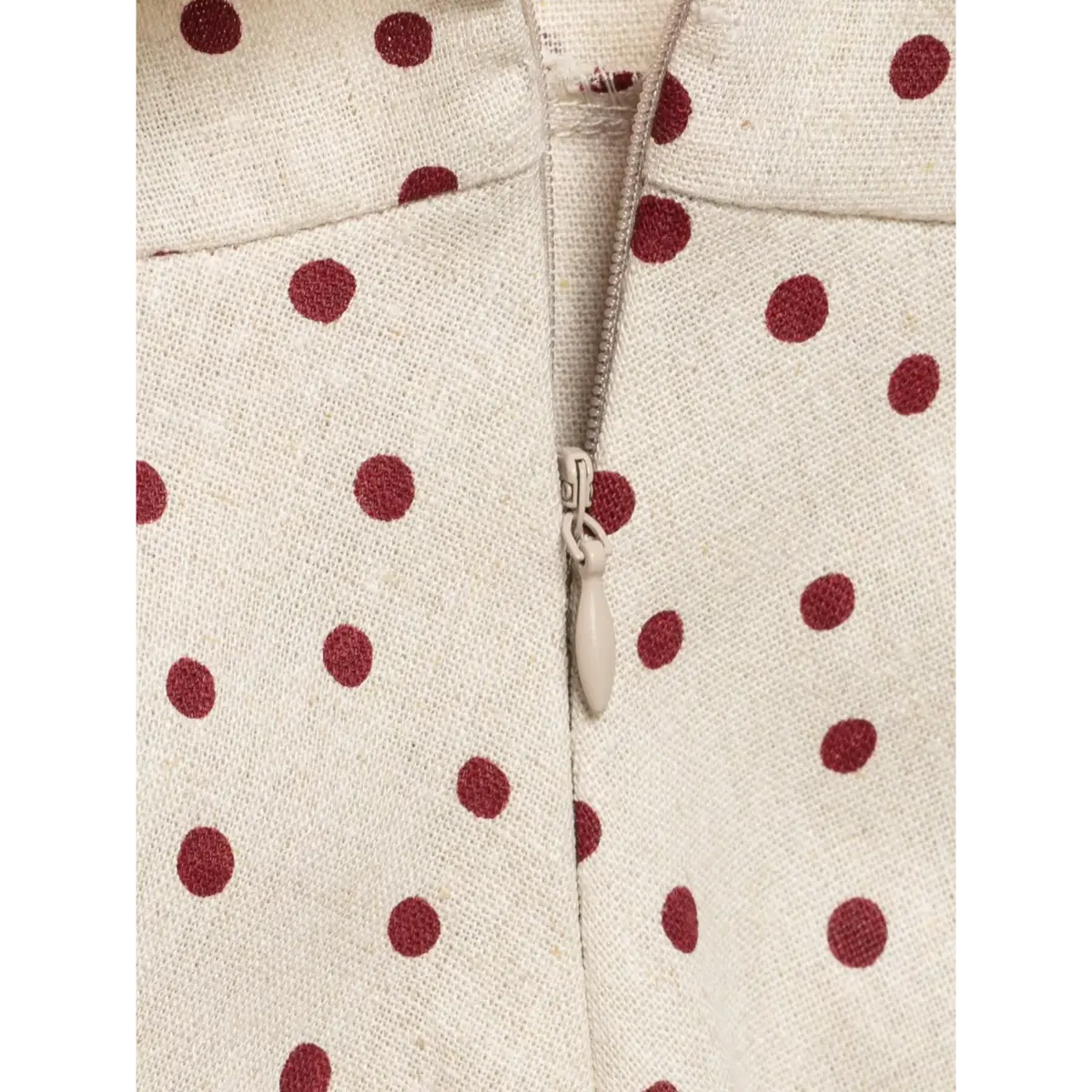 Close-up of the back zipper on a beige halter top with red polka dots, highlighting the fabric texture and zipper pull.