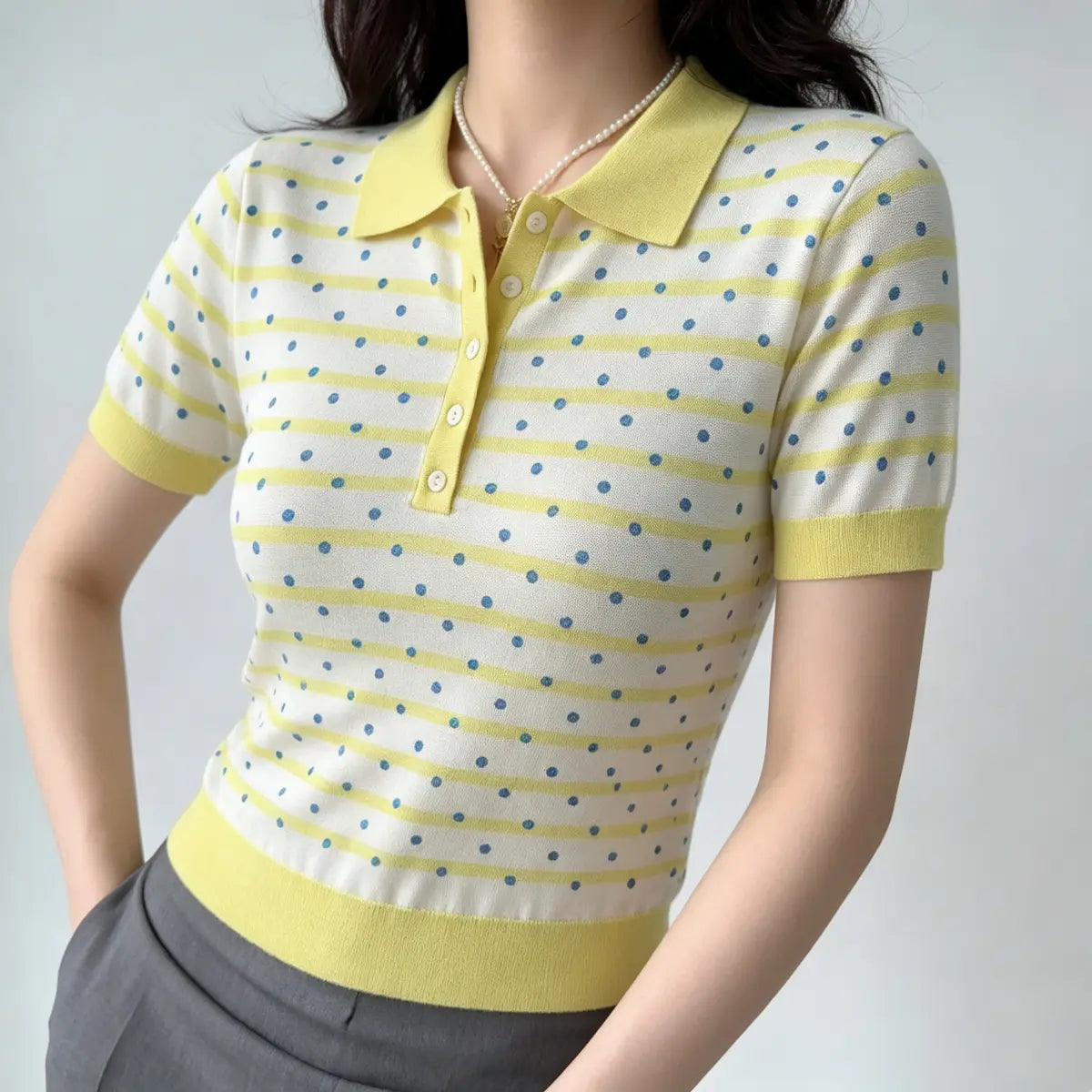 Model wearing a yellow and white polka dot knit polo shirt, showcasing the fitted silhouette, button placket, and preppy style with grey bottoms.