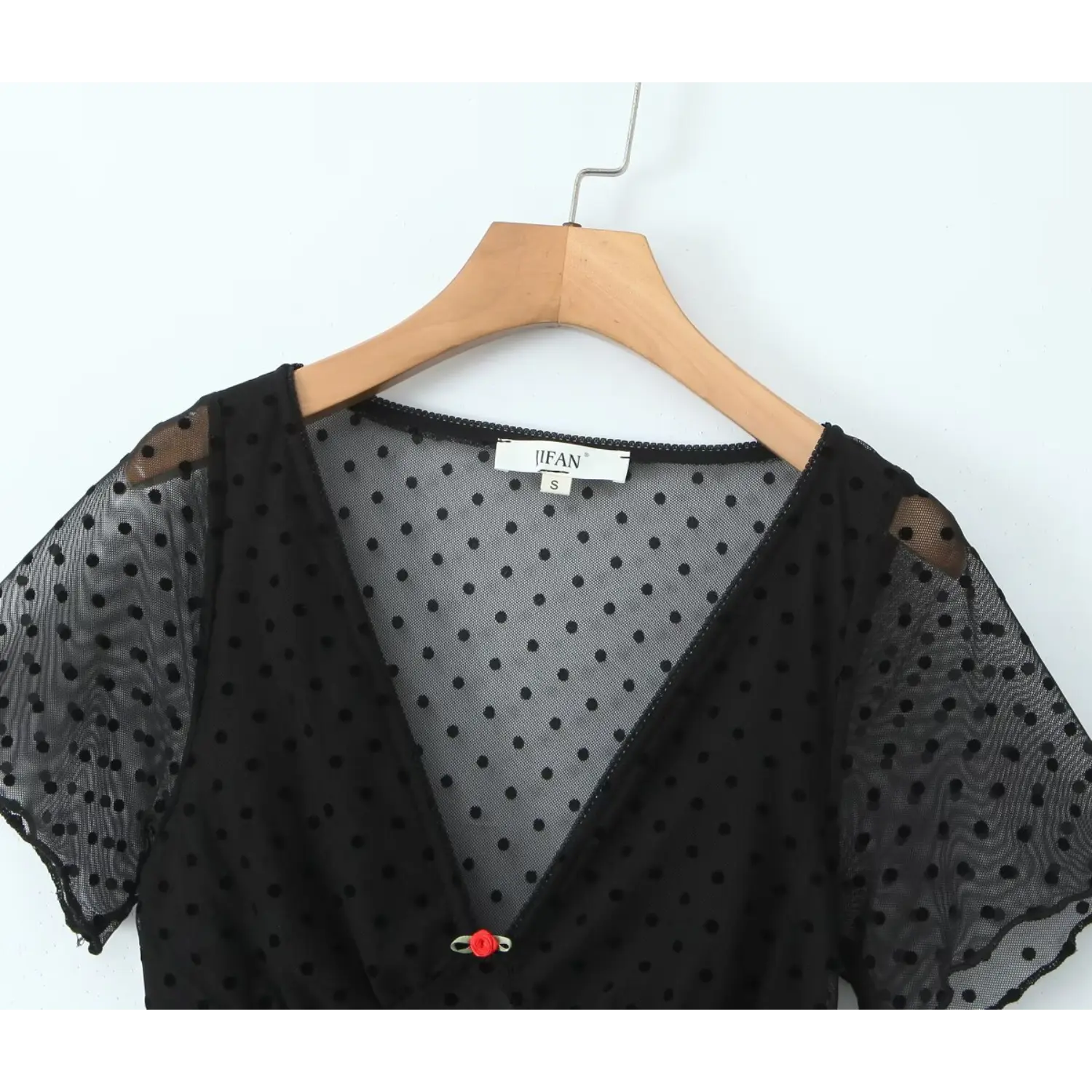 Close‑up v‑neck view of black flocked polka dot mesh dress, short sleeve and inner label detail