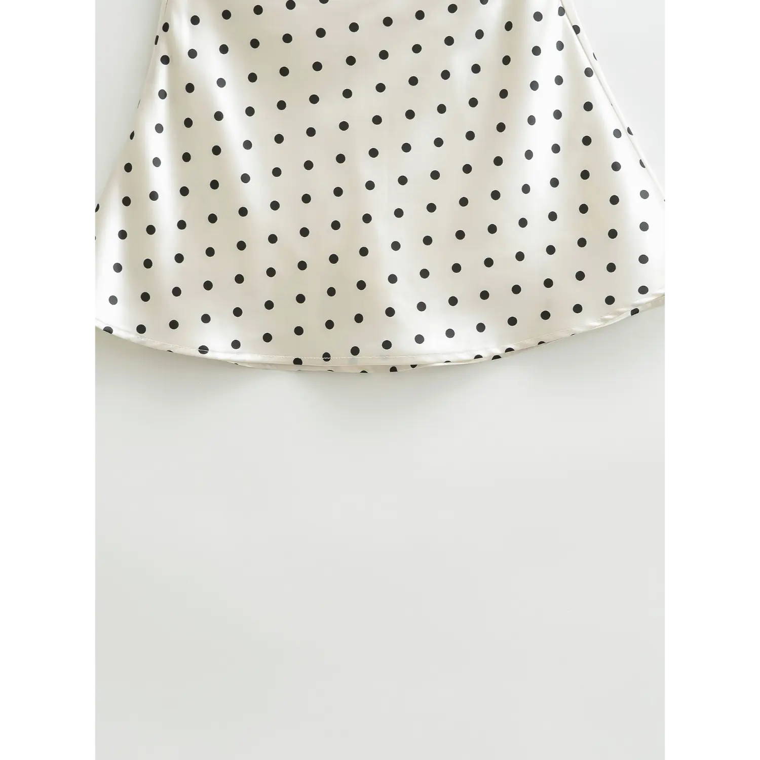 Bottom hem drape detail shot, flowy flared hem of white black polka dot glossy satin mini skirt
