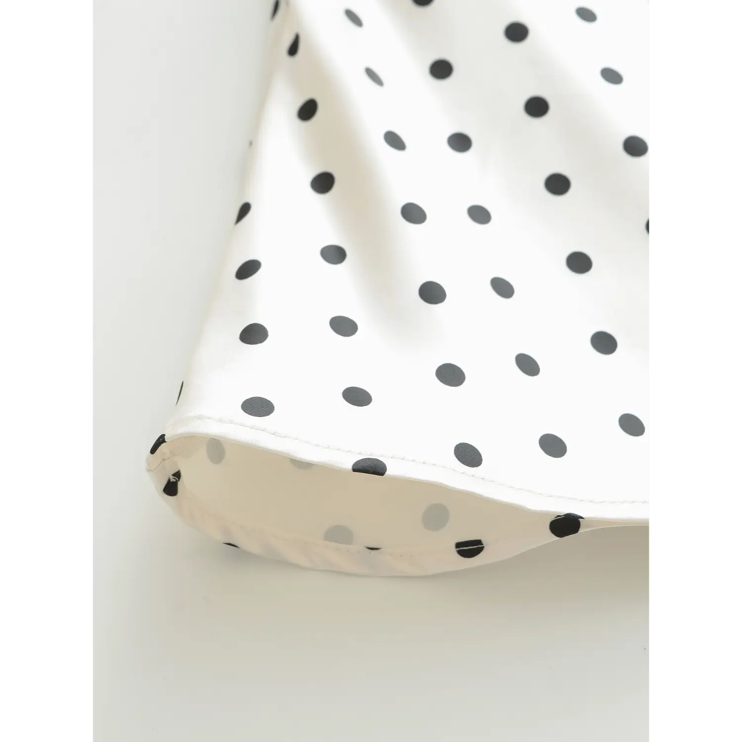 Close-up stitching detail of hem edge on white black polka dot glossy satin mini skirt