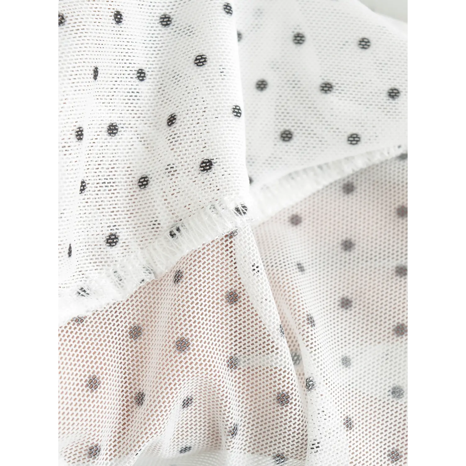 Close up texture shot of white sheer mesh fabric printed with tiny black polka dots, frilled mesh edge detail
