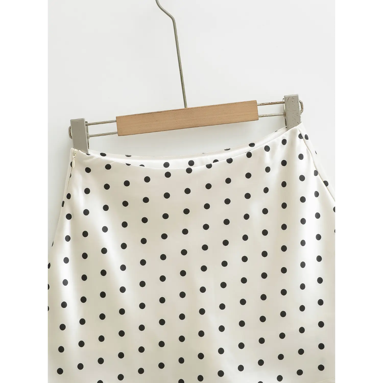 Waistband close-up detail, white polka dot satin mini skirt hanging on hanger, smooth glossy fabric texture