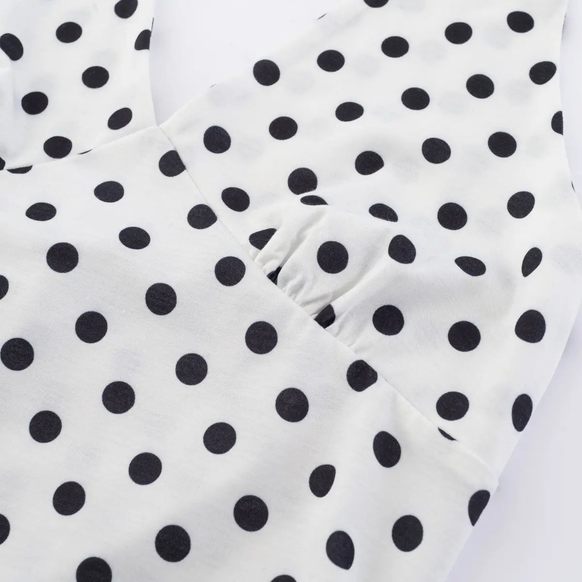 Close-up detail shot of the gathered bust on a white halter tank top with black polka dots, showing stitching and fabric texture.