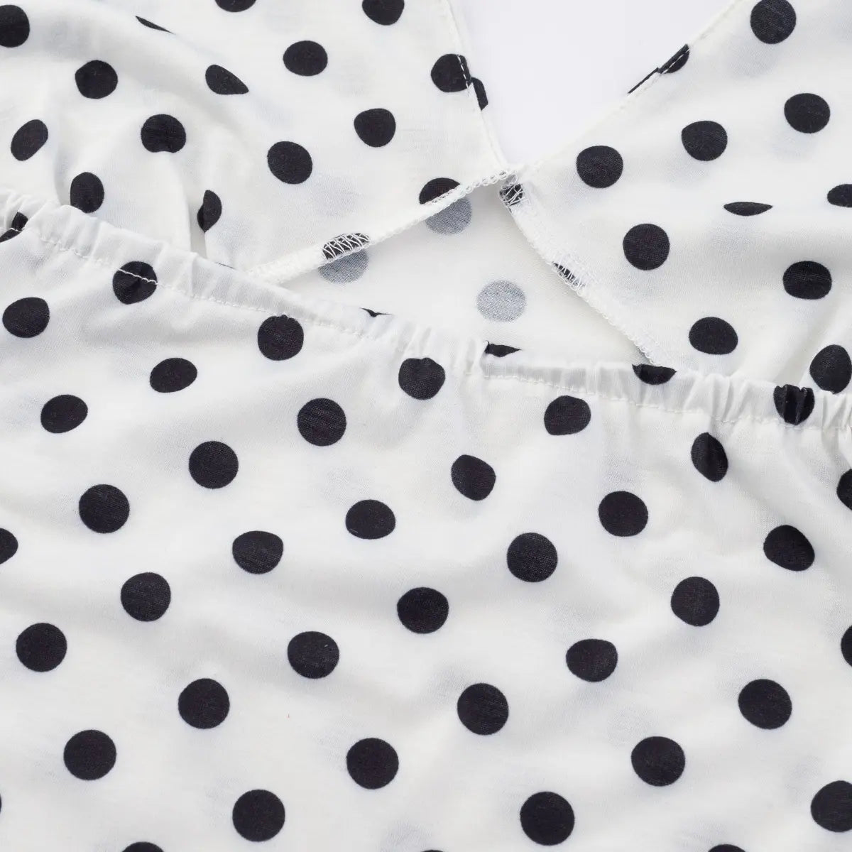 Close-up detail shot of the gathered bust seam on a white halter tank top with black polka dots, showing elastic stitching and construction.