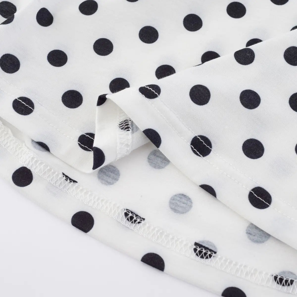 Close-up detail shot of the bottom hem and seam on a white polka dot halter tank top, showing stitching and fabric construction.