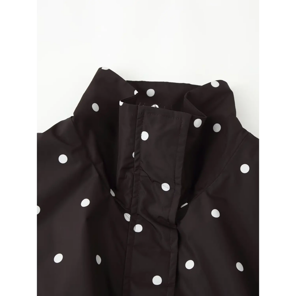 Close‑up view of stand collar and front placket on black white polka dot windbreaker, detailed stitching