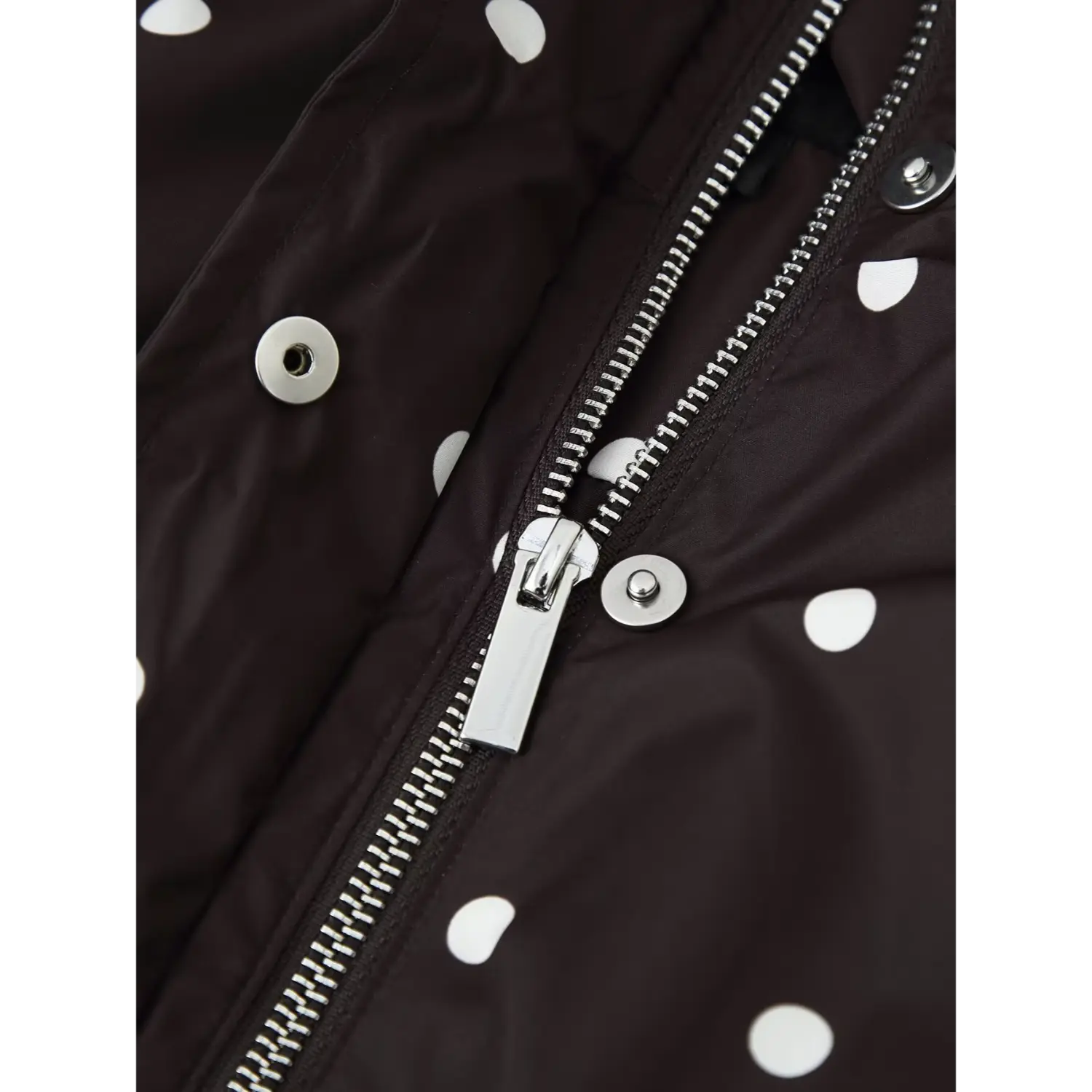 Metal zipper and snap button hardware close‑up on black polka dot windbreaker