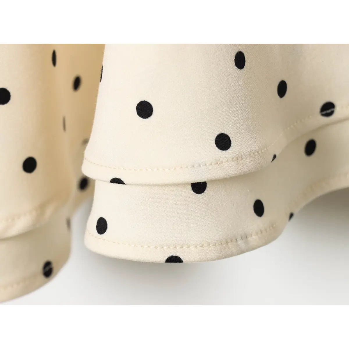 Hem close shot of dotted mini dress, double layered ruffle hem with neat finished edge stitching on smooth twill fabric.