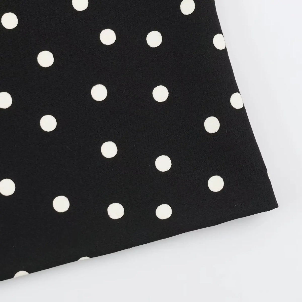 Close‑up hem detail of black midi dress with white polka dot woven fabric