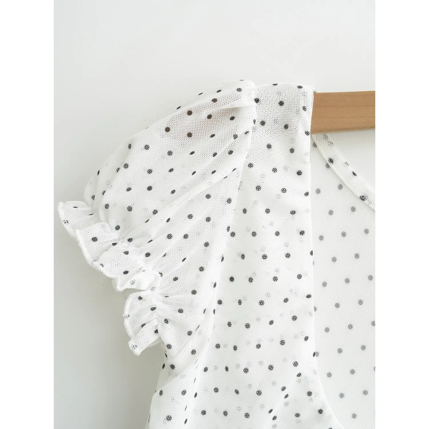 Close up shot of bubble puff sleeve with frilly ruffle trim cuff, white dot print sheer mesh top hung on wooden hanger