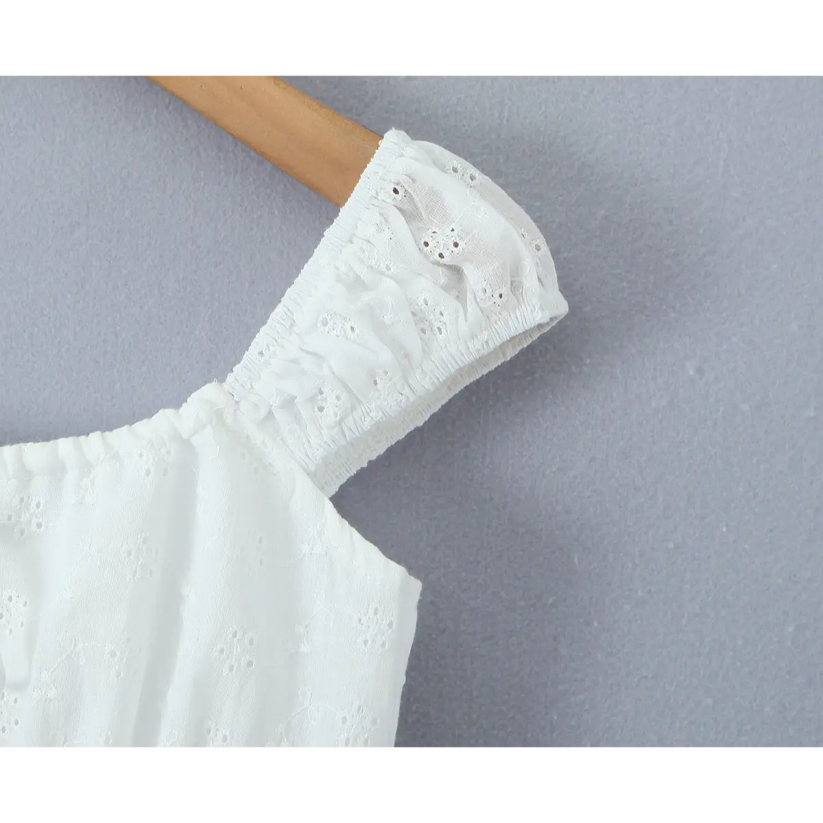 Close-up of the puff sleeve on a white eyelet embroidered top, showing the smocked elastic edge and intricate floral eyelet pattern.