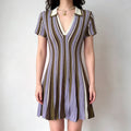 Model wearing a short-sleeve knit mini dress with vertical stripes in purple, green, and brown, featuring a contrasting white polo collar and flared skirt.