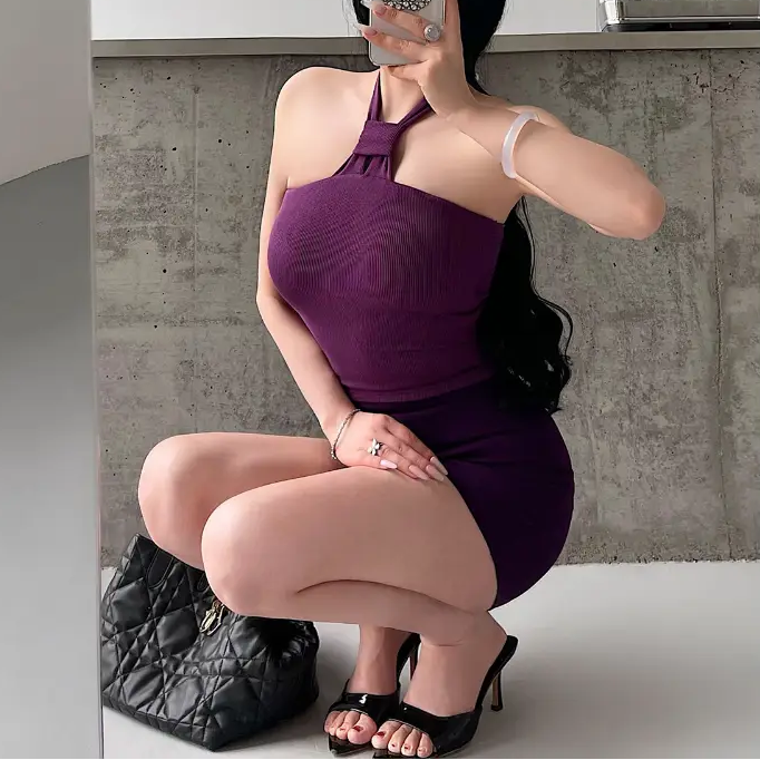  A woman wearing a purple ribbed keyhole halter top, styled with a matching mini skirt, taking a mirror selfie while squatting.