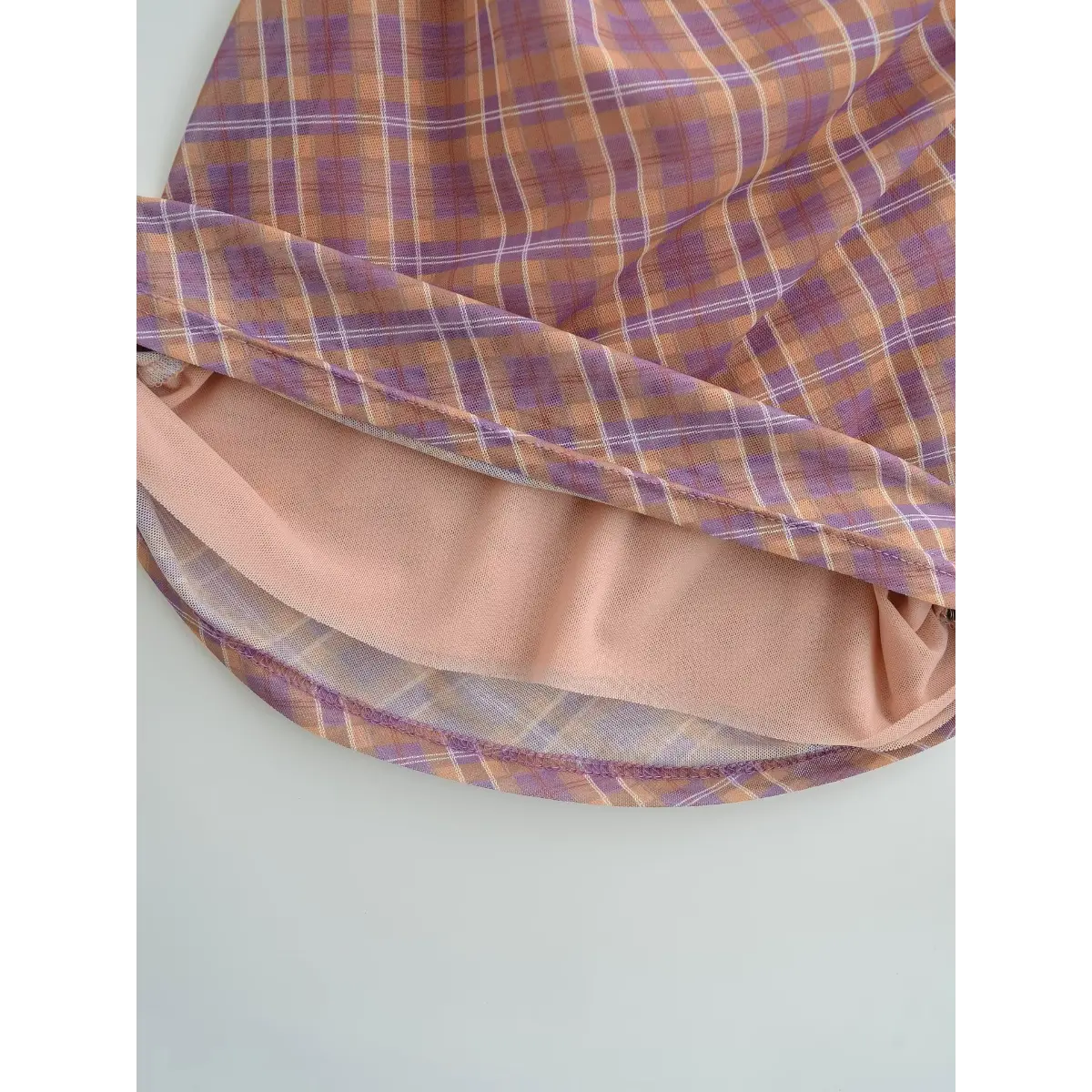 Close-up of the layered construction, showing the nude lining beneath the sheer plaid mesh.