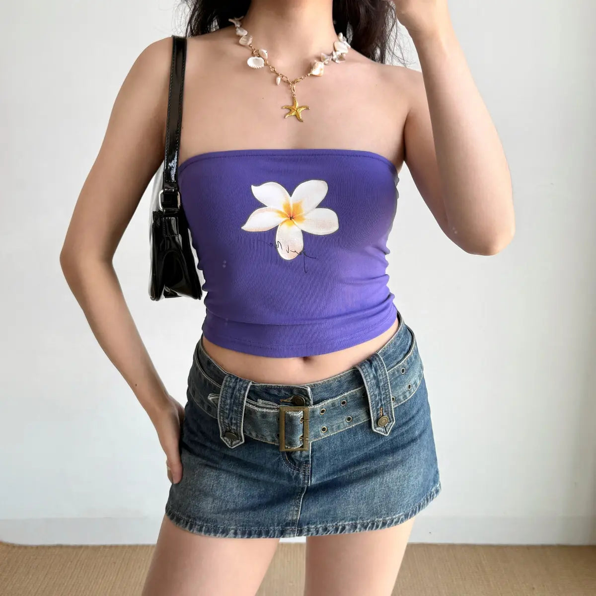 The purple plumeria-print tube top styled with a black handbag, showing the full outfit.