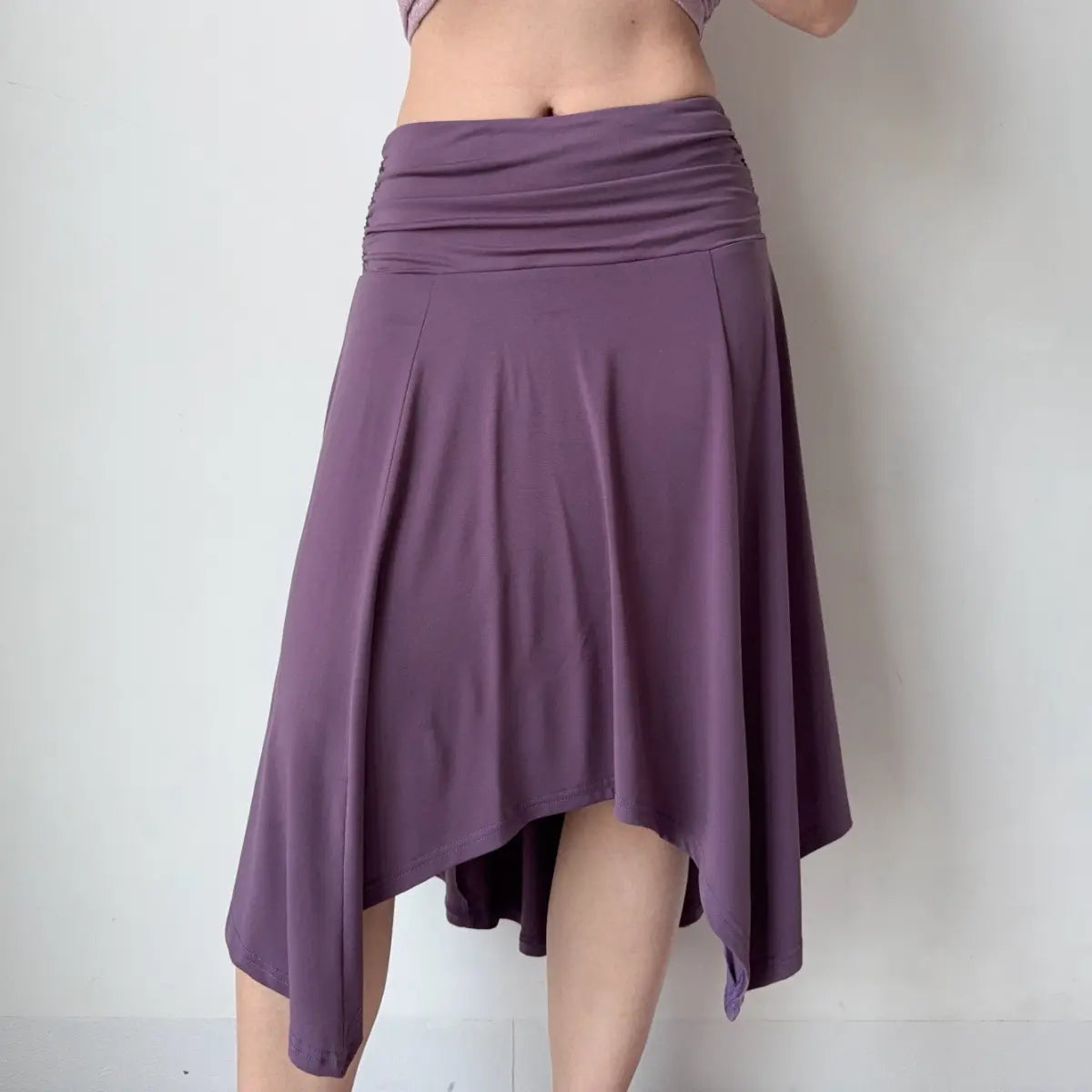 Angled view of a purple asymmetrical midi skirt, showcasing the ruched waist and dynamic, flowing silhouette.