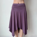 Front view of a purple asymmetrical midi skirt, showing the ruched waistband and uneven hem with soft, flowing fabric.