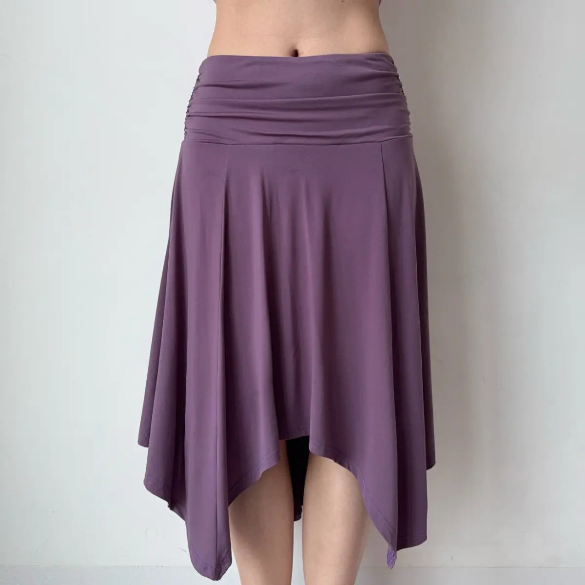 Front view of a purple asymmetrical midi skirt, showing the ruched waistband and uneven hem with soft, flowing fabric.