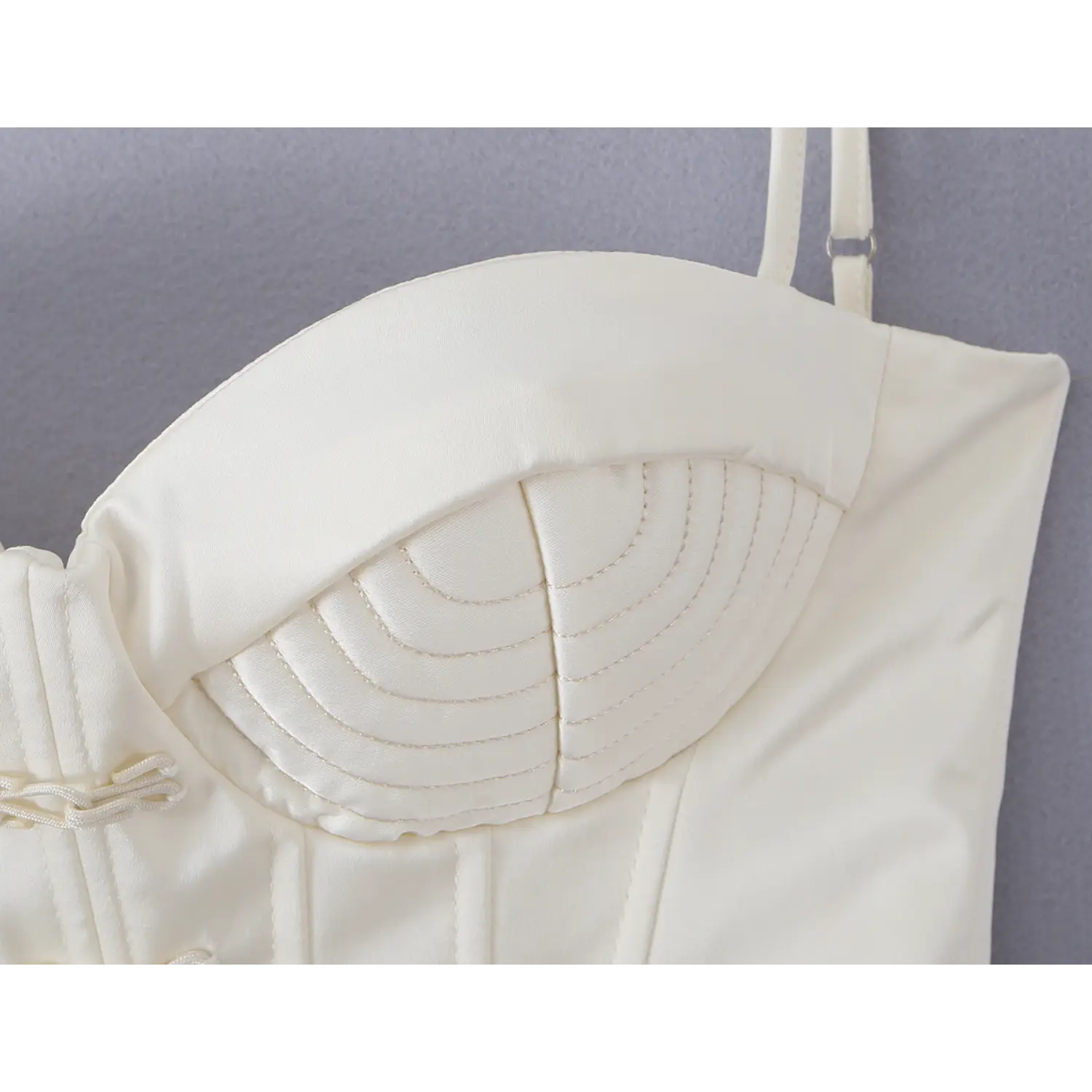 Close-up quilted stitching detail on sweetheart bust of white satin corset camisole, adjustable thin shoulder strap