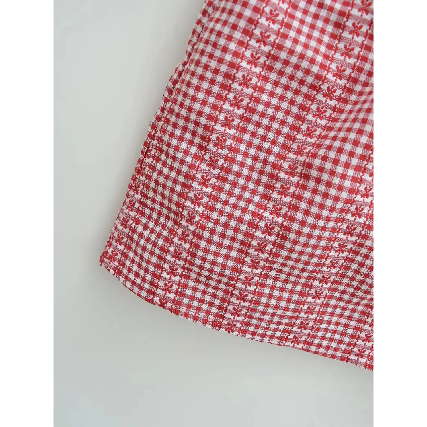 Red white tiny gingham floral cami hem macro flat shot, even small flower woven texture neat edge stitching white background detail
