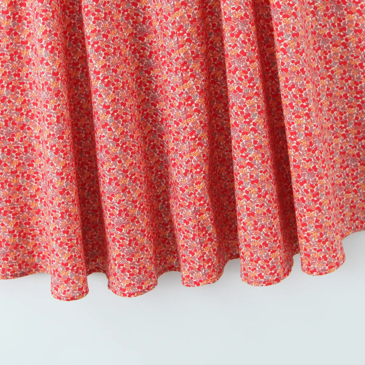 Close-up of full gathered A-line skirt hem on red cherry print halter maxi dress, lightweight flowy fabric finish.