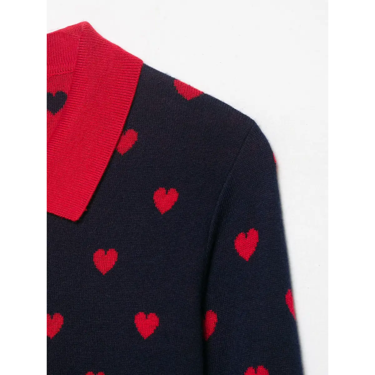  Close-up of the red ribbed collar and shoulder seam on a navy and red heart-patterned knit sweater.