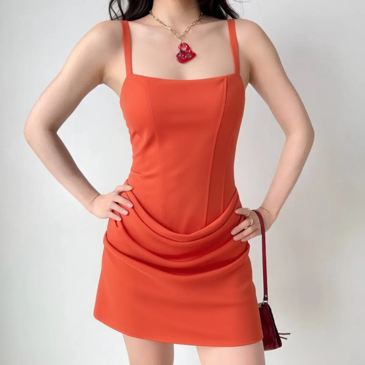 The red corset-style mini dress worn by a model, showing the fitted silhouette, draped skirt overlay, and vibrant color