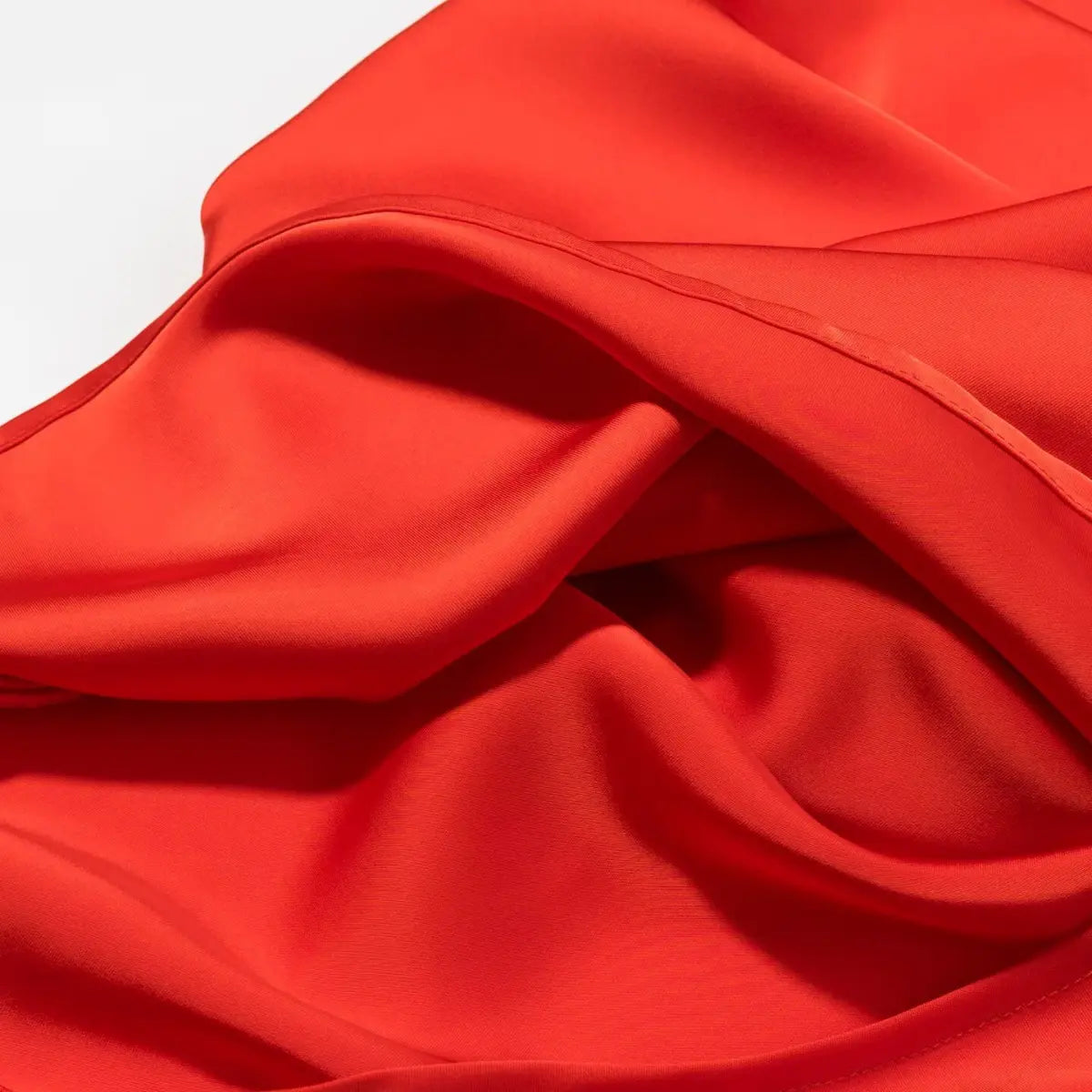 Close-up of the draped skirt fabric on the red mini dress, showing the smooth, satin-like texture and gentle folds
