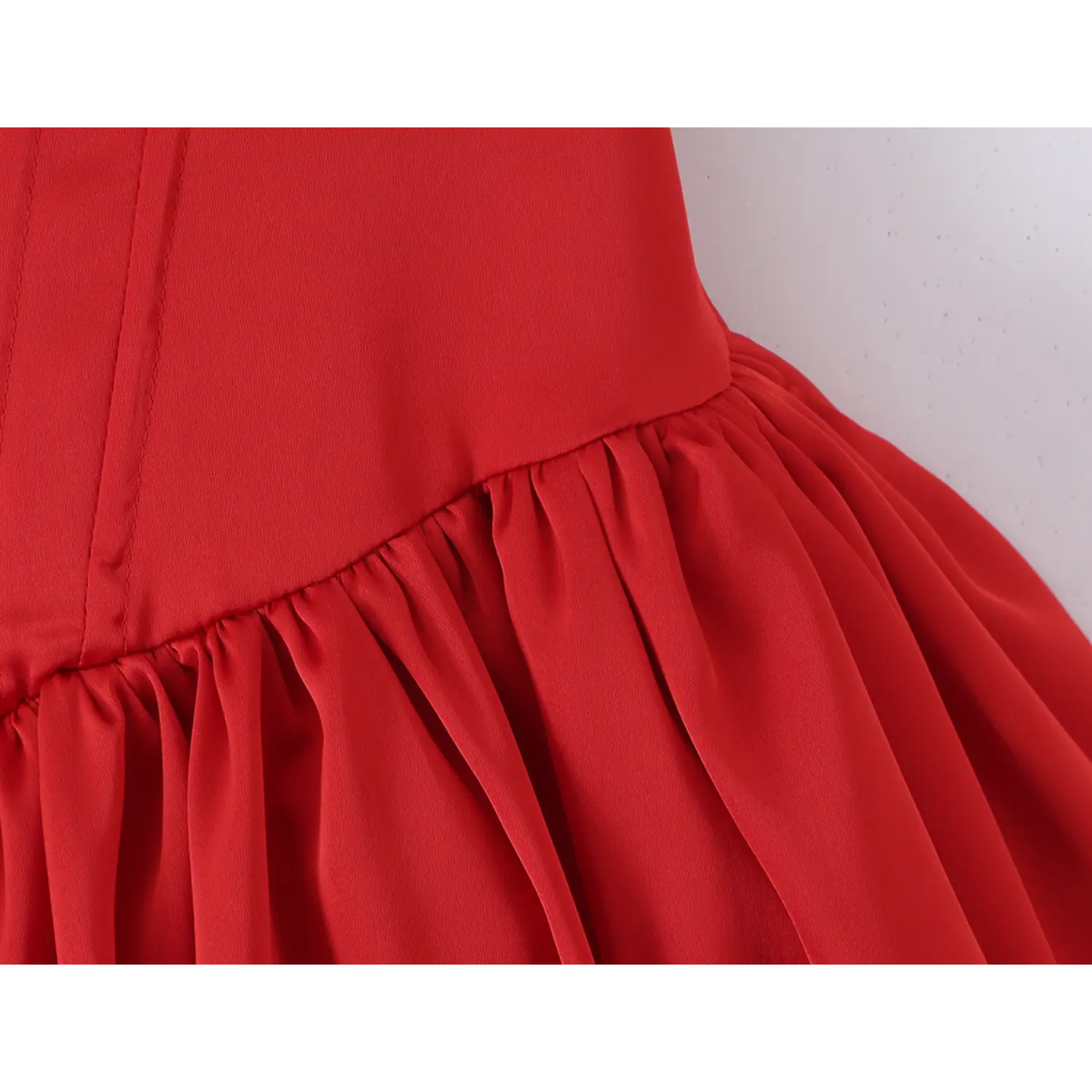 Macro close-up of stitching seam between structured corset waist and gathered satin skirt on red mini dress