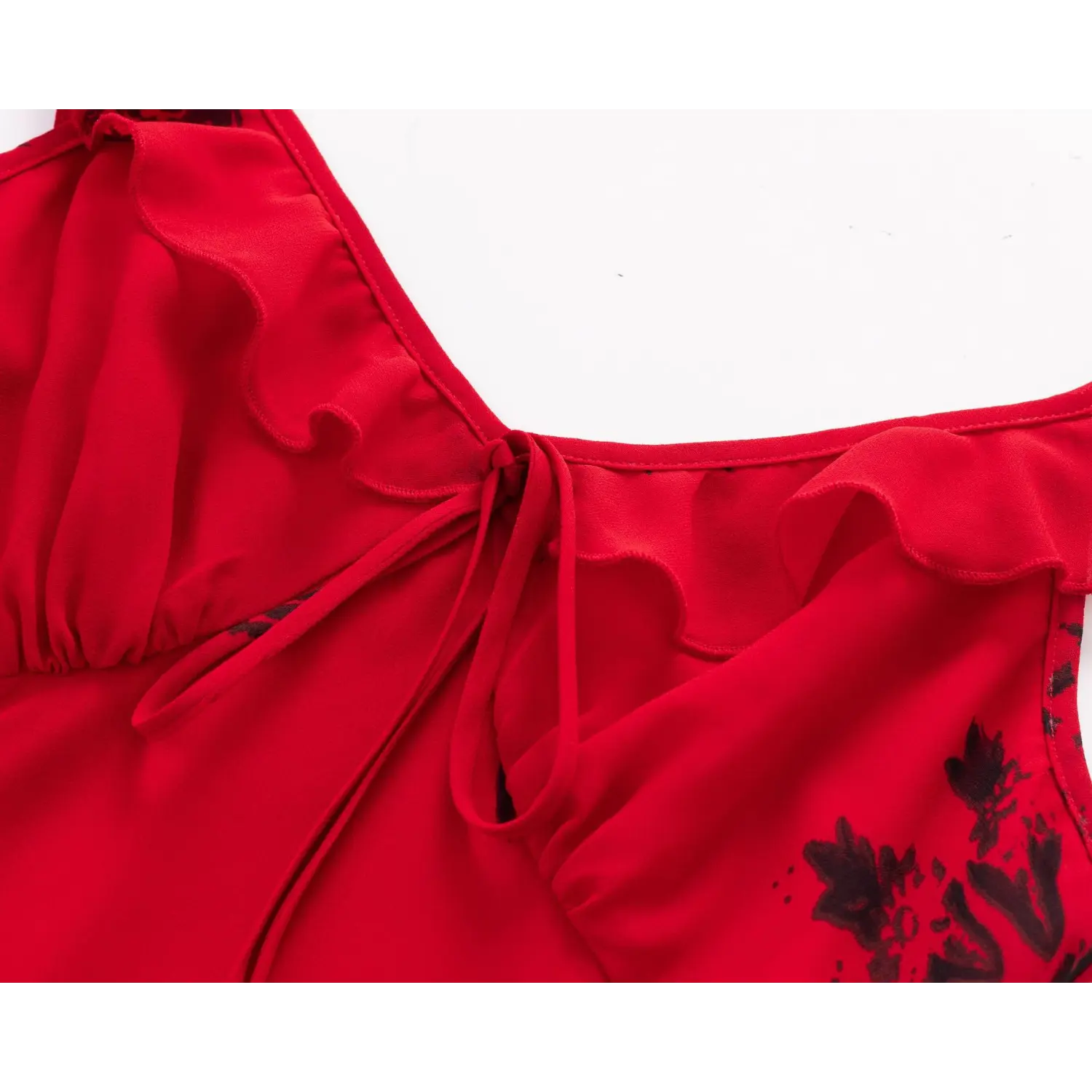 Macro close‑up of front fabric tie at bust, ruffle trim v‑neck on red black floral printed chiffon dress