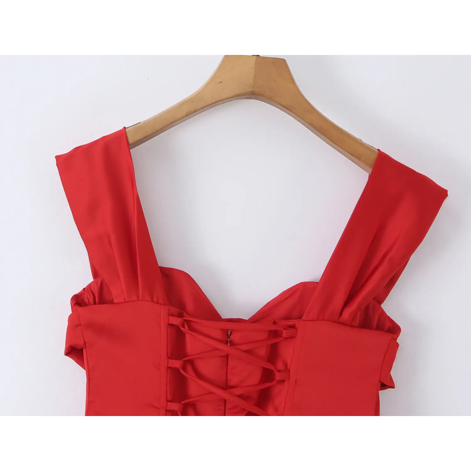 Close up detail of wide folded shoulder straps and upper criss cross lace up corset back on red satin mini dress