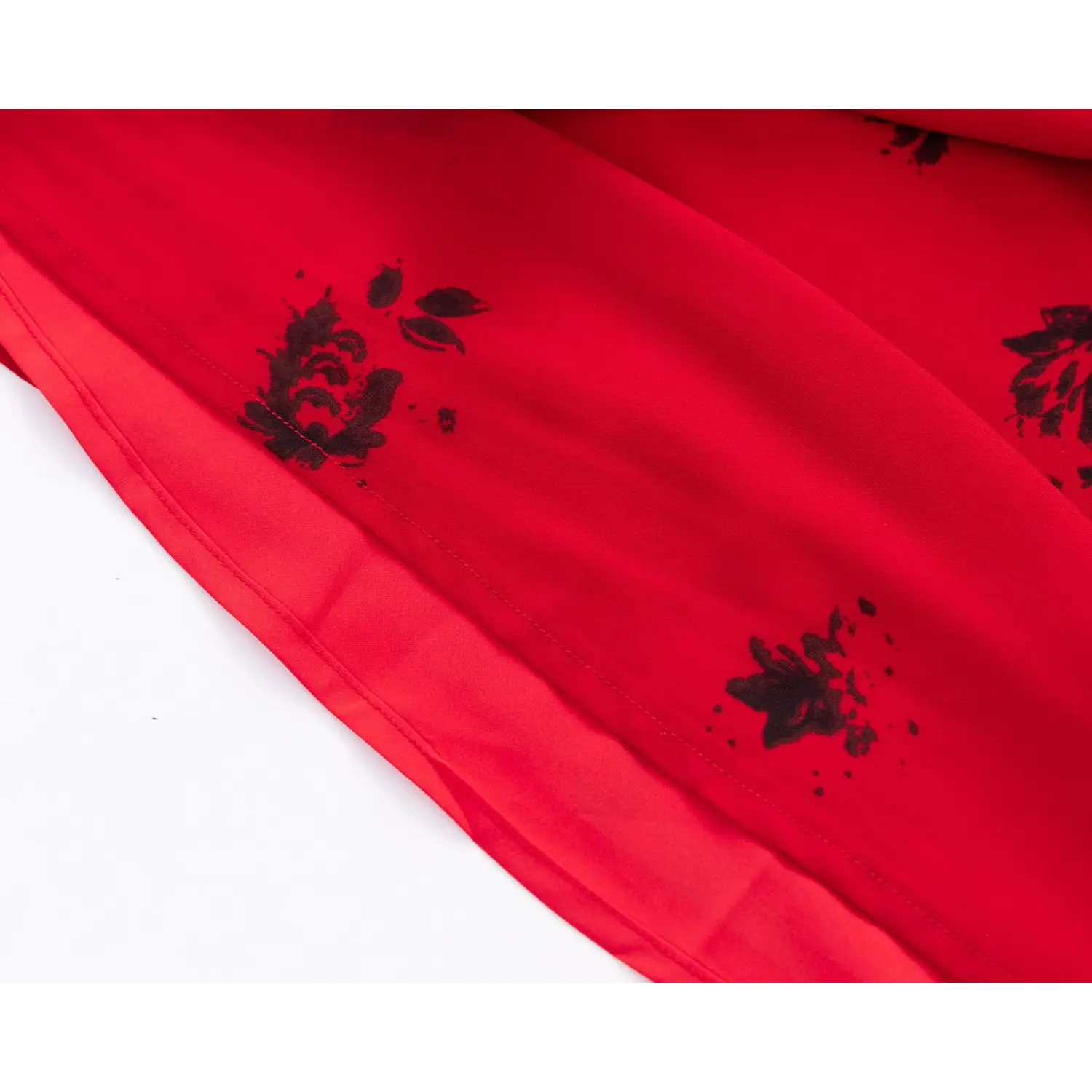 Close‑up of dress hem, chiffon outer layer and inner lining, black floral print on red fabric