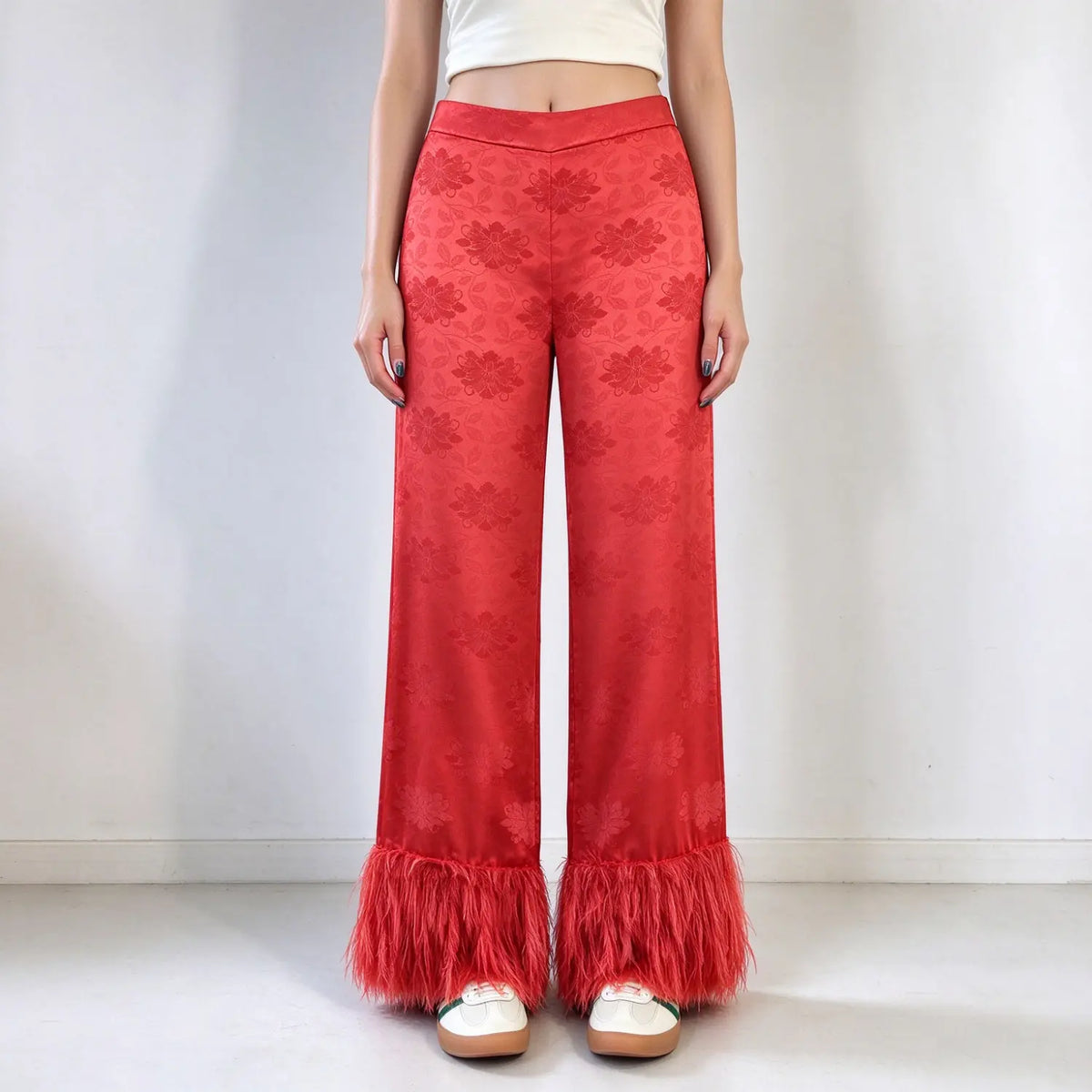 Model wearing red floral jacquard flare pants, high waist, subtle floral embossed pattern, long feather tassel hem, slim flare silhouette, paired with white cropped top, plain white background