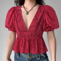 Woman styled in a red floral appliqu peplum top, featuring a deep V-neck, puff sleeves, and gathered waist, paired with blue jeans.