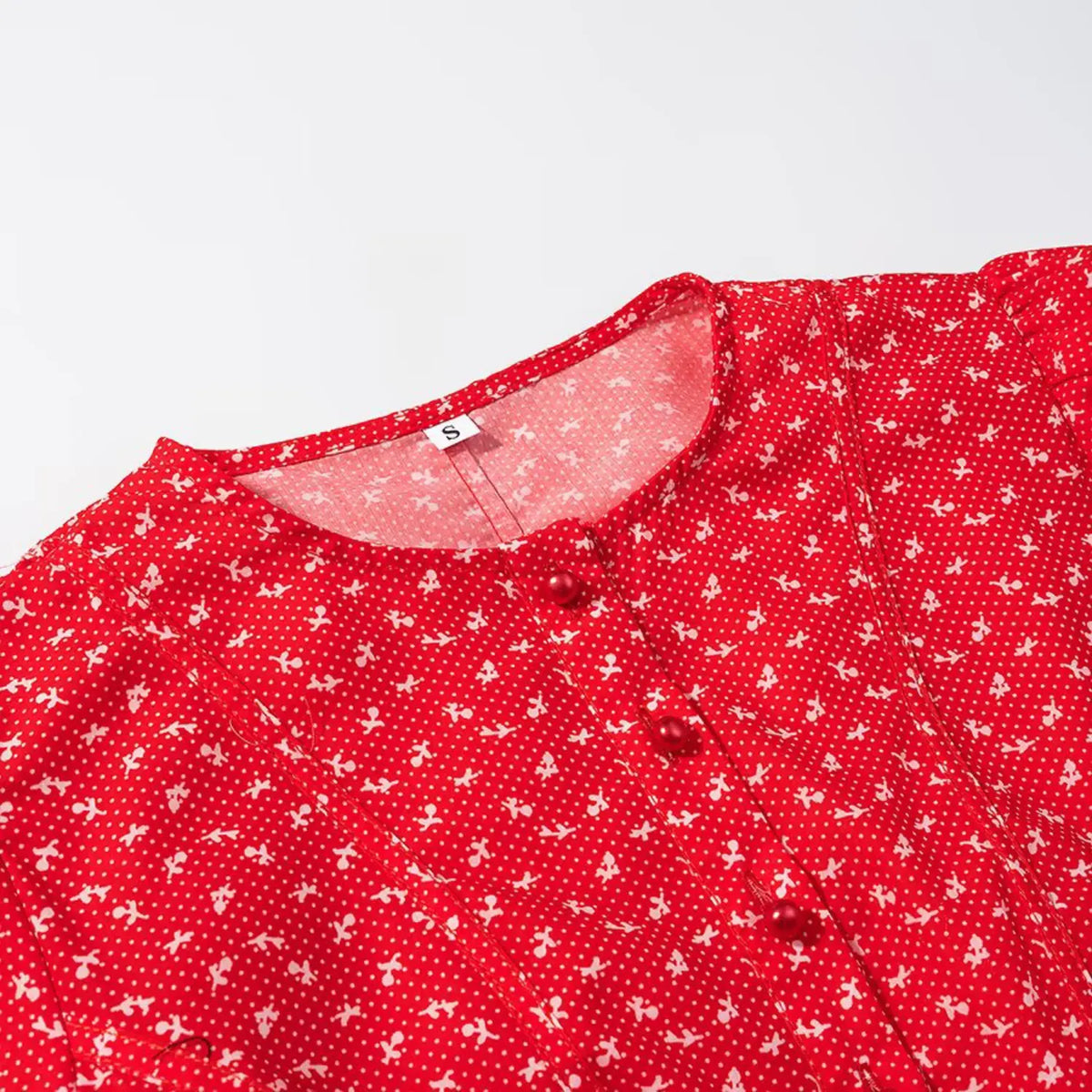 Close‑up of round neckline and red pearl buttons on red ditsy floral cropped top