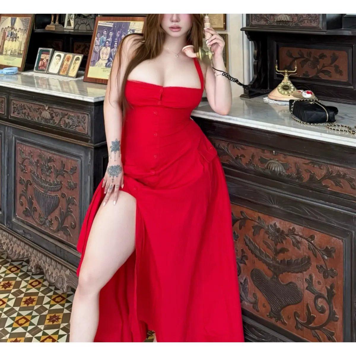 Woman in a bright red halter maxi dress posing in an antique shop, leaning against a carved wooden cabinet with vintage decor.