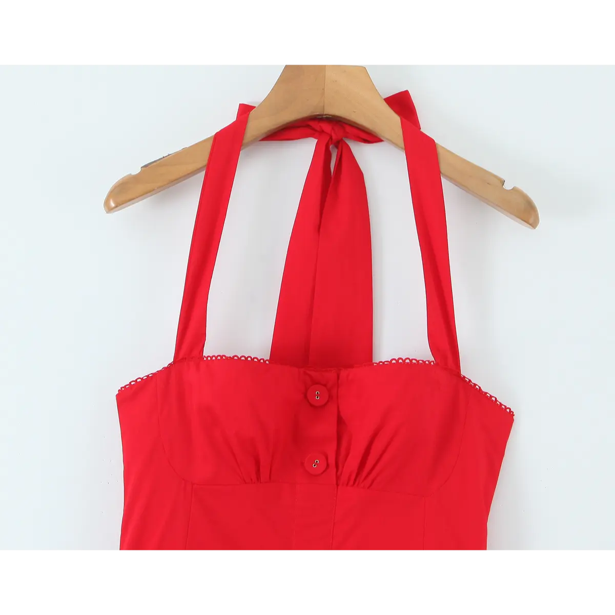 Close-up of the front bodice of a bright red halter maxi dress, featuring the halter tie, matching red buttons, and scalloped neckline trim.