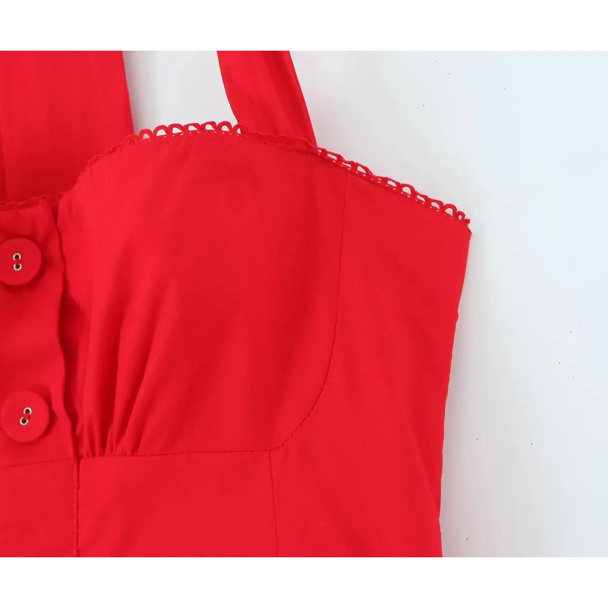  Close-up of the front bodice of a bright red halter dress, featuring scalloped lace trim, gathered fabric, and matching red buttons.
