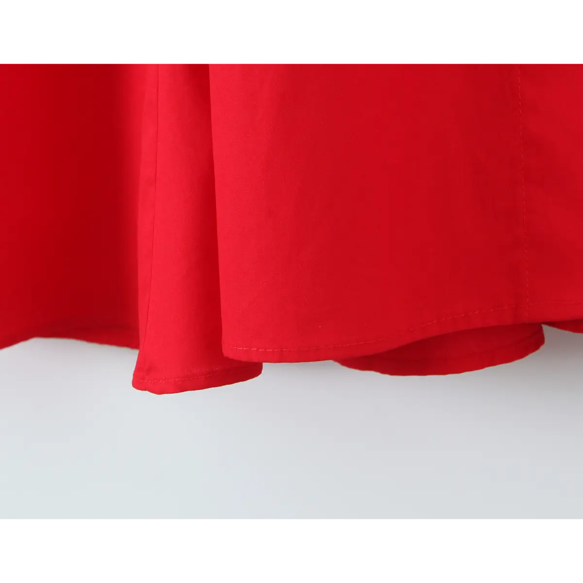 Close-up of the finished hem of a bright red halter maxi dress, showing the double-layered construction and clean stitching.