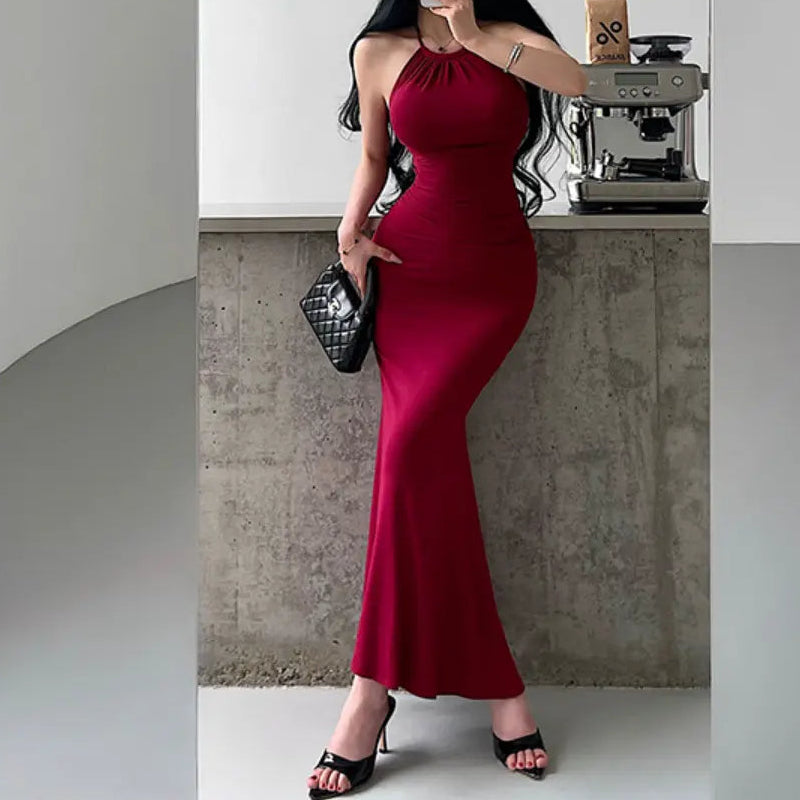 A woman wearing a red halter-neck mermaid maxi dress with ruched waist and bodycon fit, styled with black accessories.