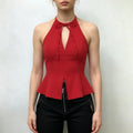 Model wearing red halter peplum top, front tie‑bow keyhole cutout, fitted bodice with flared split peplum hem