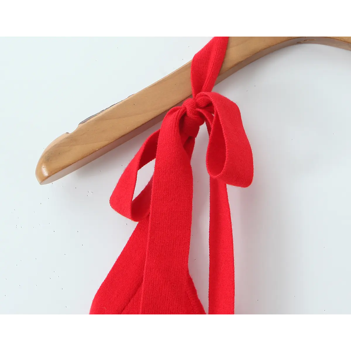  Close-up of self-fabric knotted bow tie on halter strap, matching red knit fabric accessory detail.