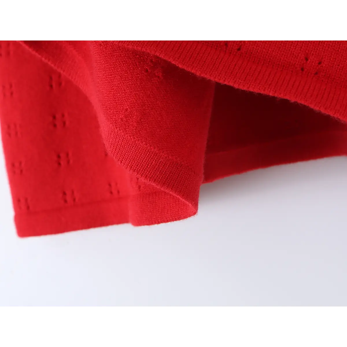 Close-up of red knit fabric, showing the eyelet pattern and scalloped, ribbed hem.