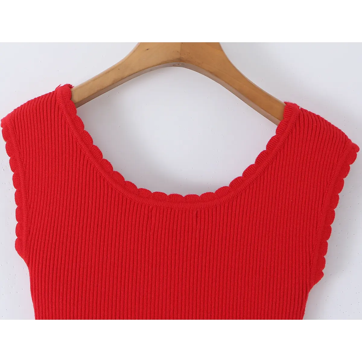 Close-up of the back neckline on a red knit dress hung on a wooden hanger, showing the scalloped edge and ribbed knit fabric.