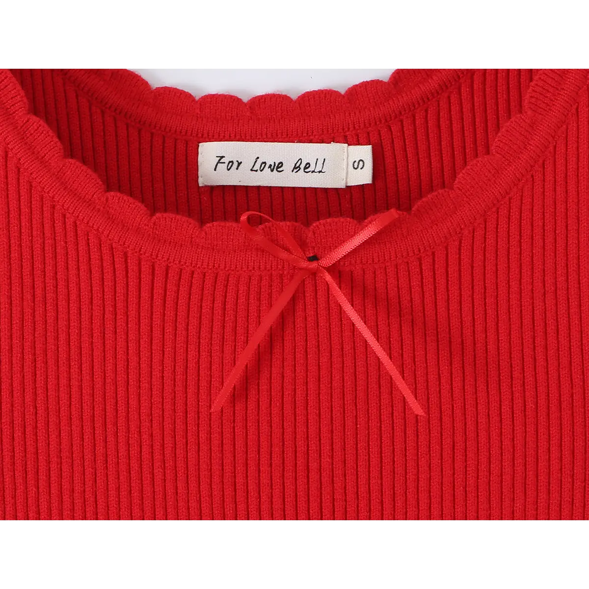 Close-up of the brand label on a red knit dress, reading "For Love Bell," next to the scalloped neckline and center ribbon bow.