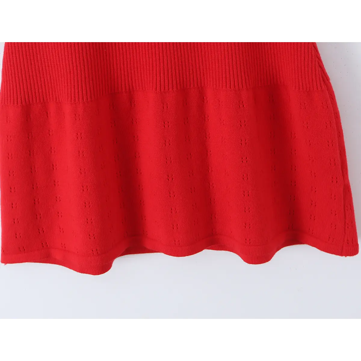 Close-up of the skirt hem on a red knit dress, showing the ribbed waistband, eyelet knit pattern, and scalloped hem.