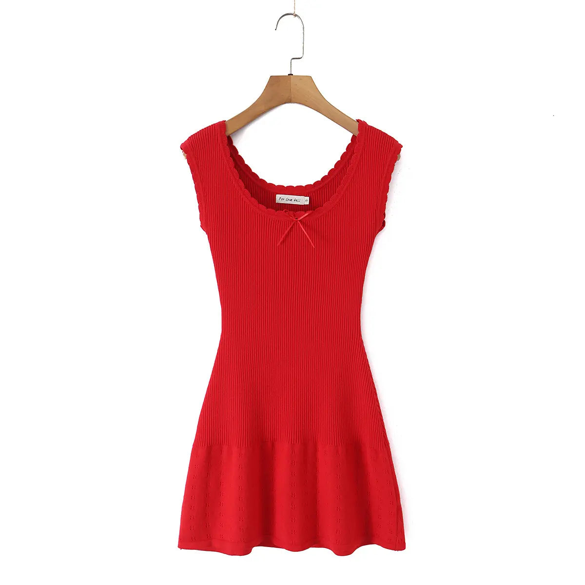 Studio shot of a red ribbed knit mini dress hung on a wooden hanger, featuring scalloped edges and a center ribbon bow.