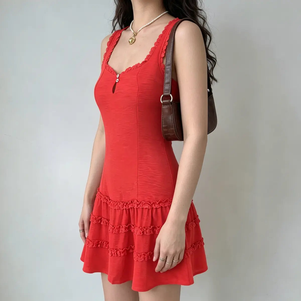 Side view of a model wearing a red lace-trim tiered mini dress with keyhole neckline, carrying a brown shoulder bag.