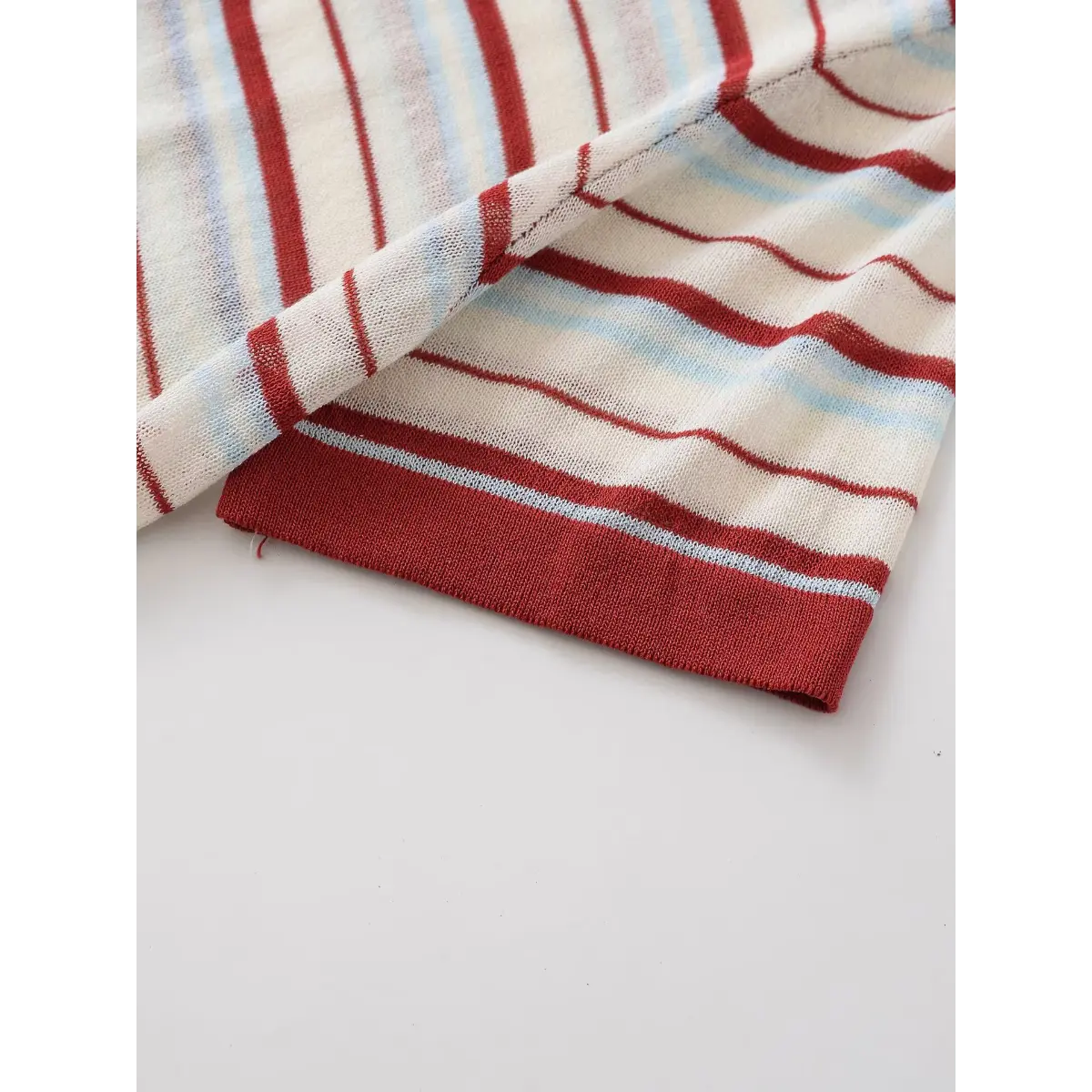 Sleeve cuff detail of the red and light blue striped knit top, showing the ribbed trim and semi-sheer fabric
